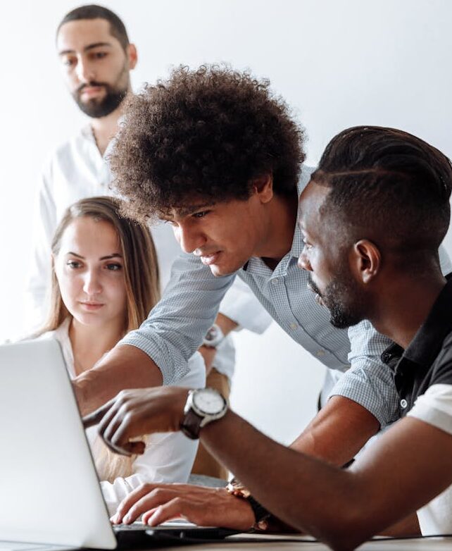 Group of professionals engaging in a collaborative discussion around a laptop in a modern office setting.